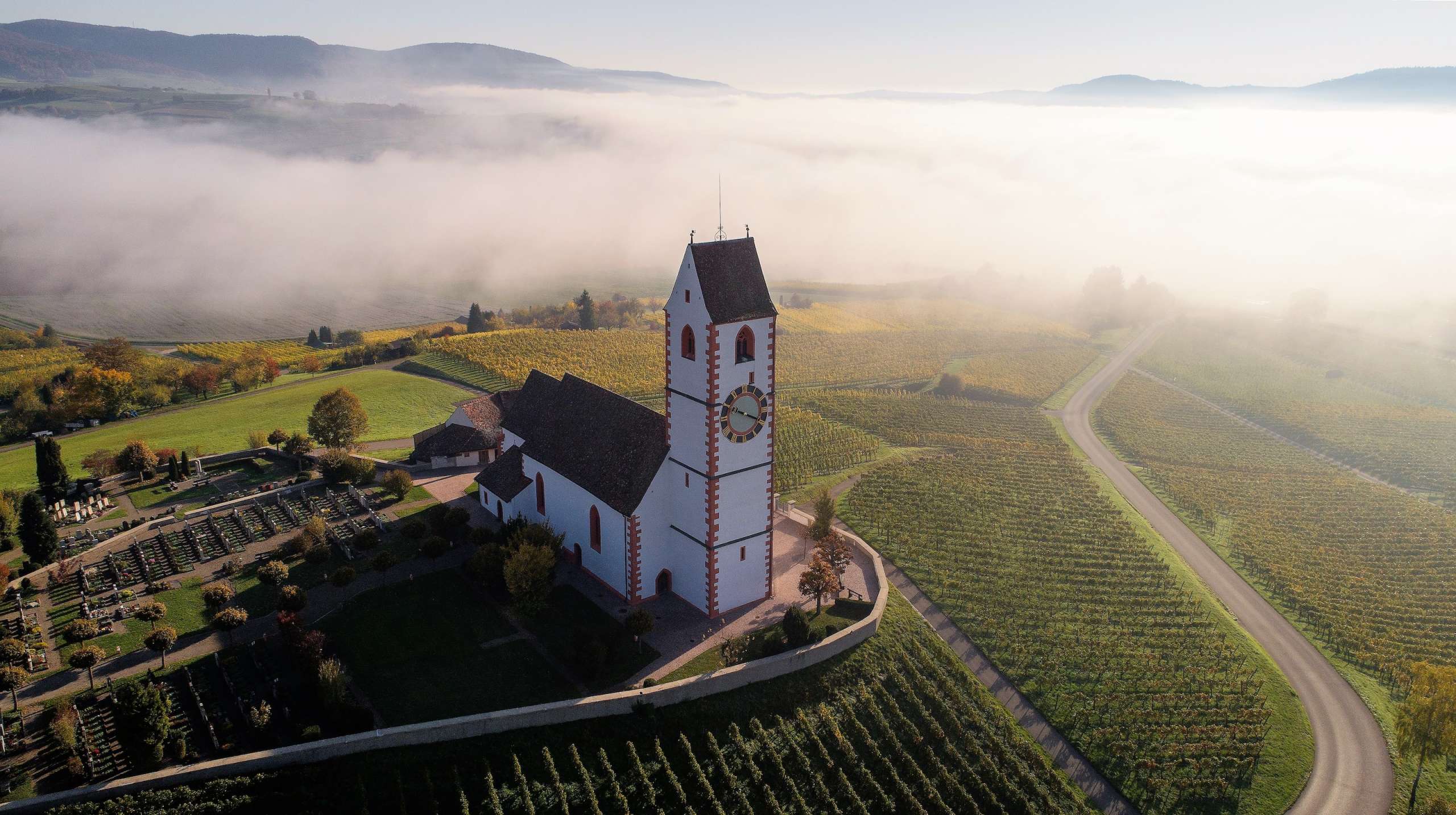 Während das Dorf Hallau in Nebel getaucht ist, ragt die Bergkirche an diesem Herbsttag stolz über den Nebel hinaus.